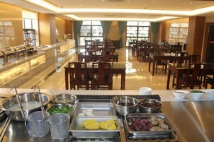 Un bufé con diversos alimentos y utensilios, dispuesto en un amplio comedor con mesas y sillas.