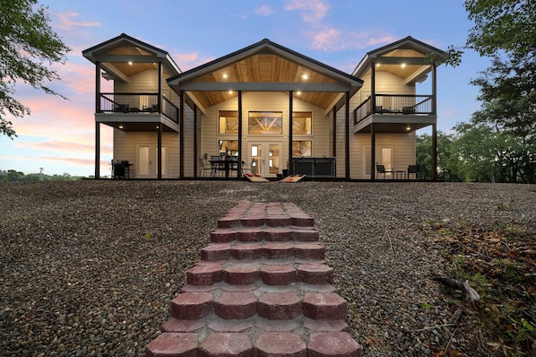 A two-story building with a covered front porch, multiple balconies, and a gravel pathway leading to the entrance. - Riverfront/HeatedPool/Arcade/Kayak/Tube (Broken Bow)