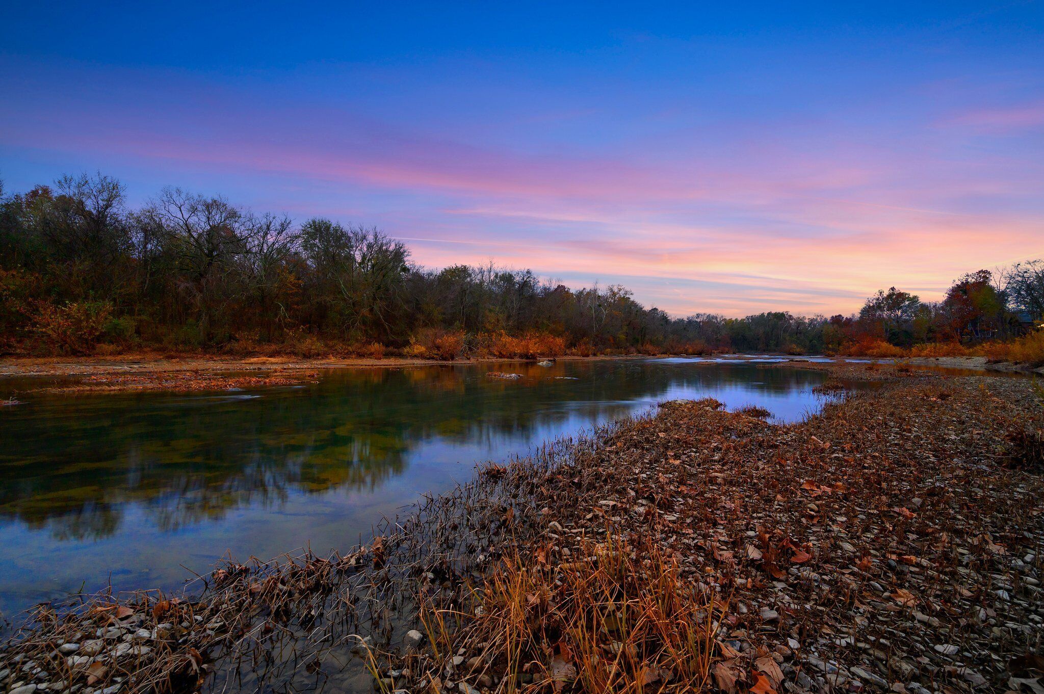 A river with a rocky shore and trees in the background.