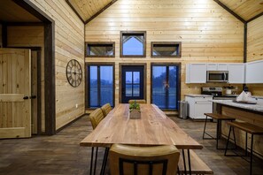 A wooden interior with a long dining table, chairs, a clock, and a kitchen area with a microwave and stove. - Riverfront/HeatedPool/Arcade/Kayak/Tube (Broken Bow)