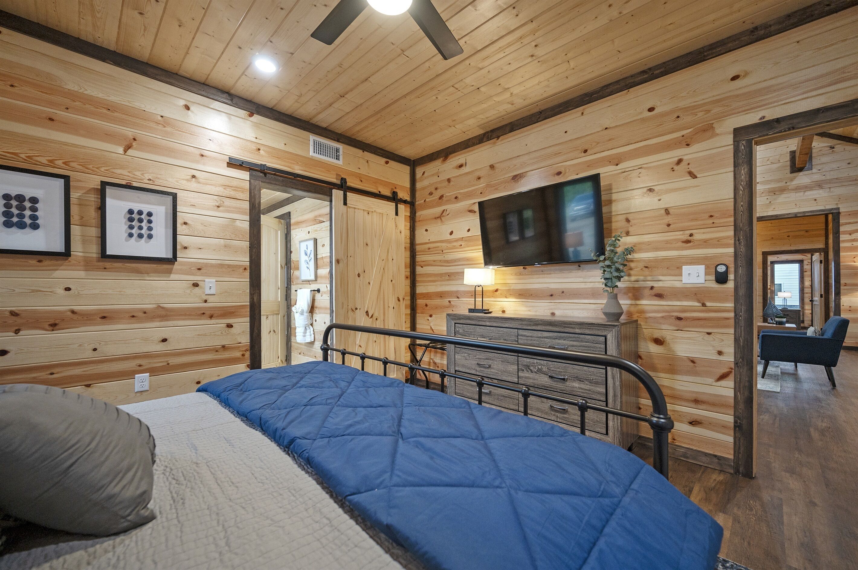 Habitación con paneles de madera, una cama, un aparador, un televisor y una puerta que da a otra habitación.