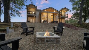Une maison à deux étages avec un foyer en pierre au centre, entouré de fauteuils Adirondack en bois.