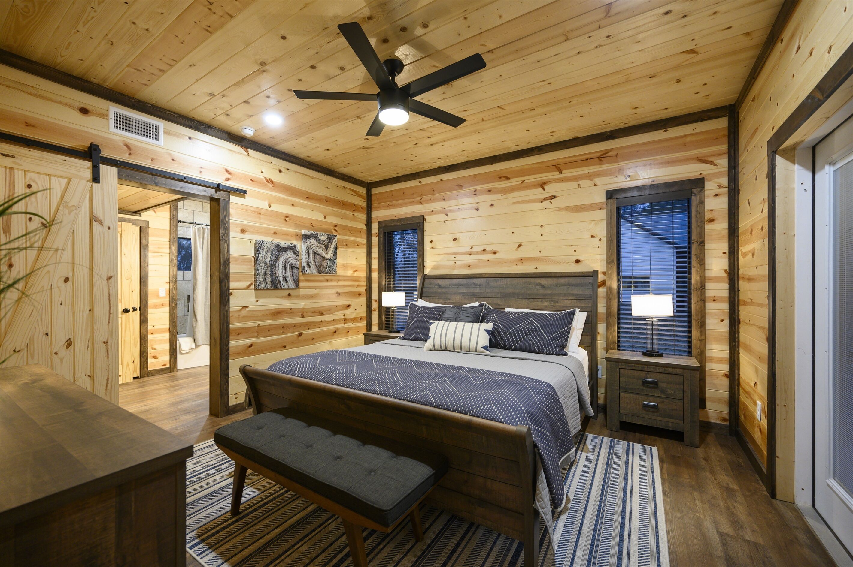 A wooden cabin bedroom with a bed, bench, bedside tables, and a ceiling fan.