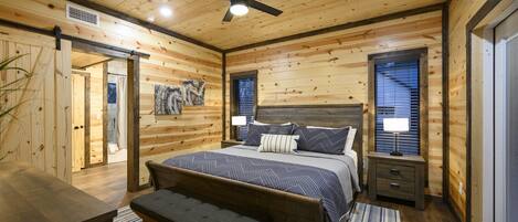 A wooden cabin bedroom with a bed, bench, bedside tables, and a ceiling fan.