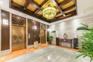 A hotel lobby with a marble floor, wooden panel ceiling, and a reception desk with a vase and a clock. - Xiyue wanda Hotel (Xiuyan)