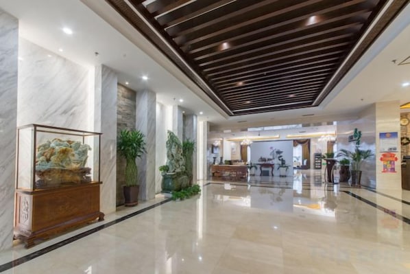 A hotel lobby with marble columns, a reception desk, and potted plants.