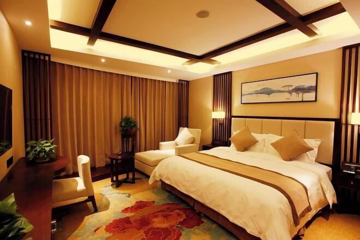 Une chambre d’hôtel avec un grand lit, deux chaises, un bureau et un tableau au mur.