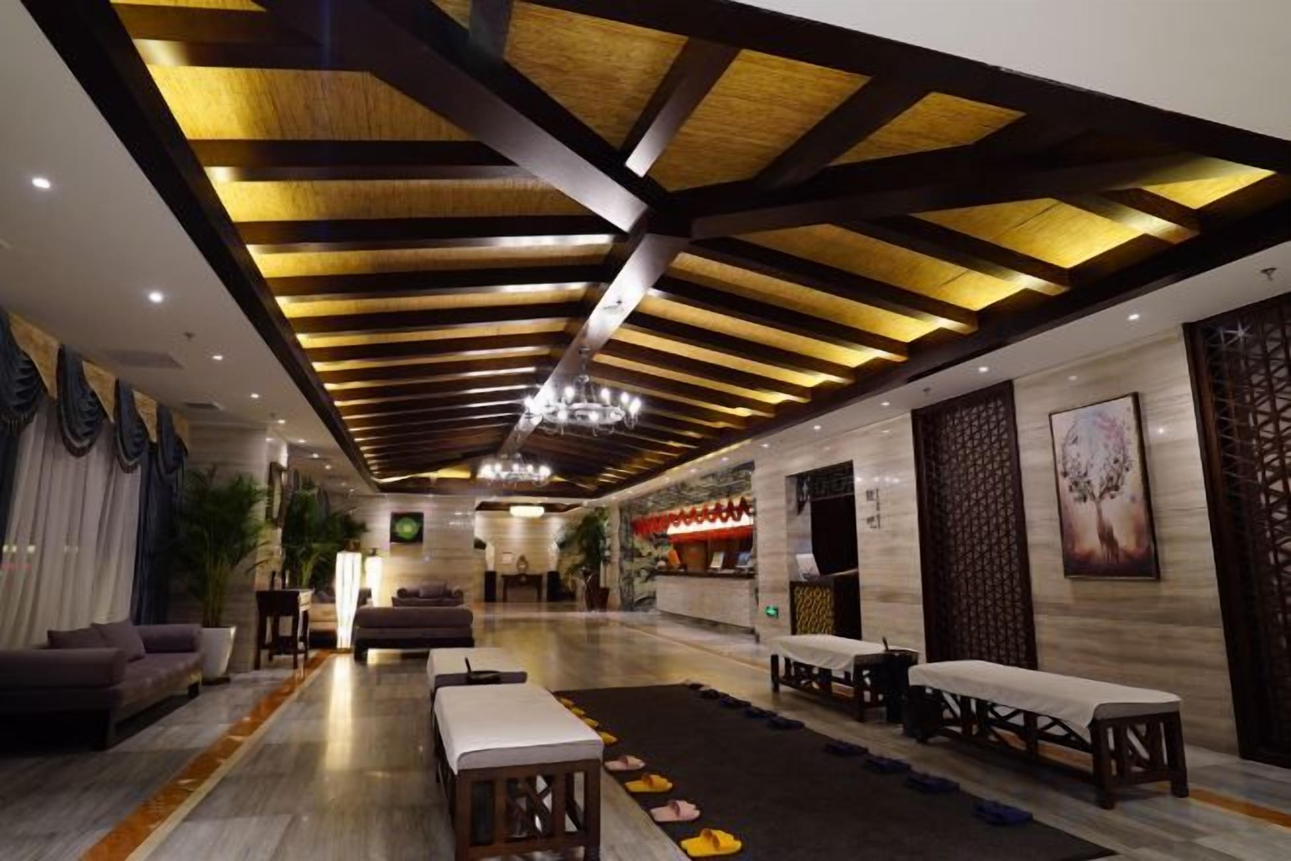 A hotel lobby with a high ceiling, wooden beams, and a chandelier. There are seating areas with tables and chairs.