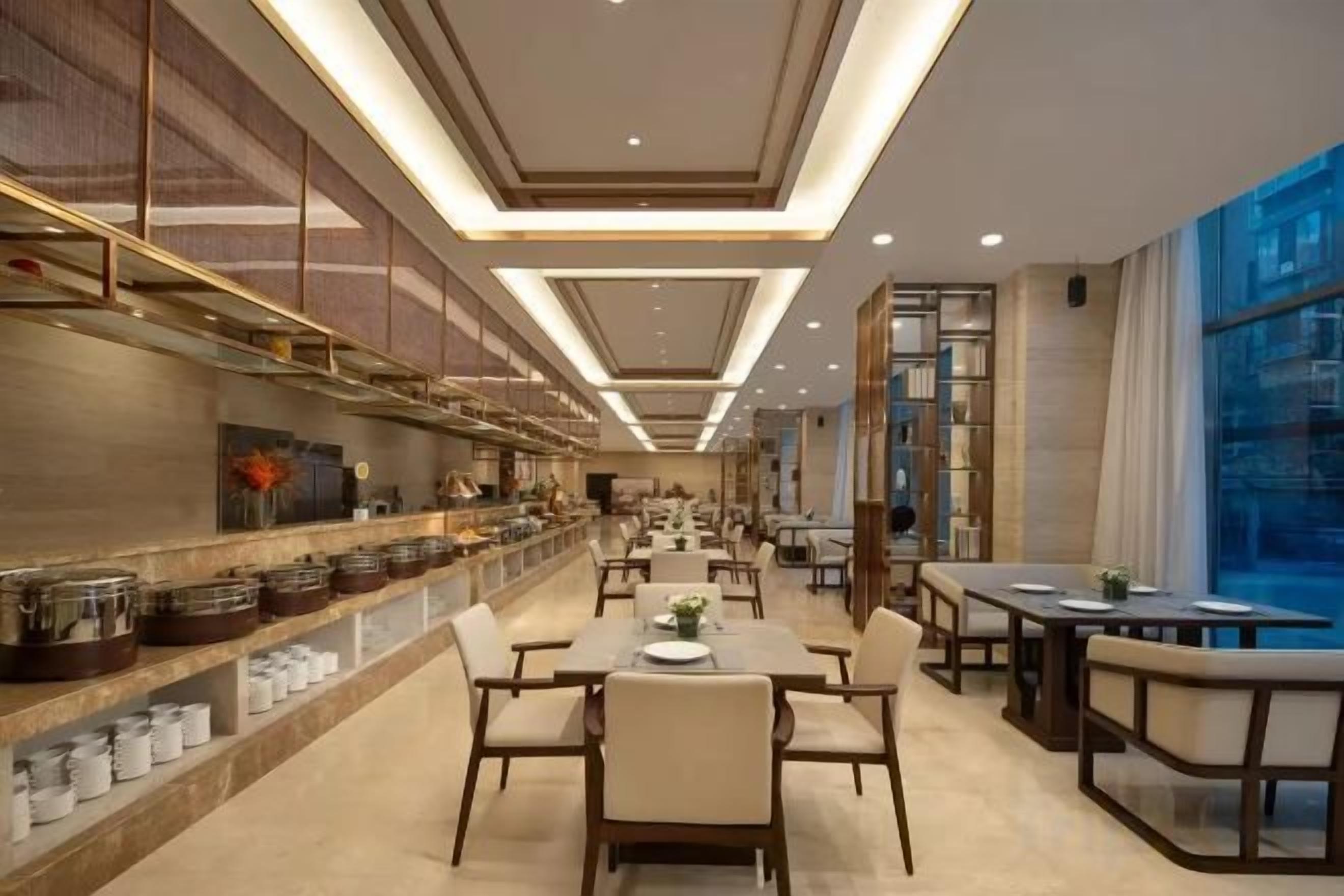 A modern restaurant with a long counter, multiple tables, and a high ceiling with recessed lighting.