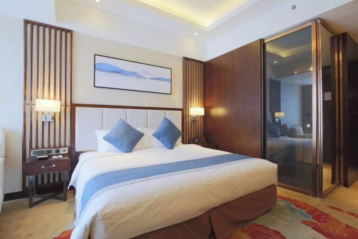 Une chambre d’hôtel avec un grand lit, une table de chevet, une lampe fixée au mur, un tableau encadré et une porte coulissante.