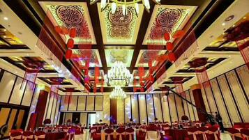 Un salón de banquetes con mesas y sillas dispuestas en filas, una araña y decoraciones geométricas en el techo.