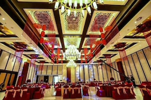 Un salón de banquetes con mesas y sillas dispuestas en filas, una araña y decoraciones geométricas en el techo.
