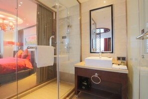Een moderne badkamer met een douchecabine van glas, een wit wastafeltje en een grote spiegel.