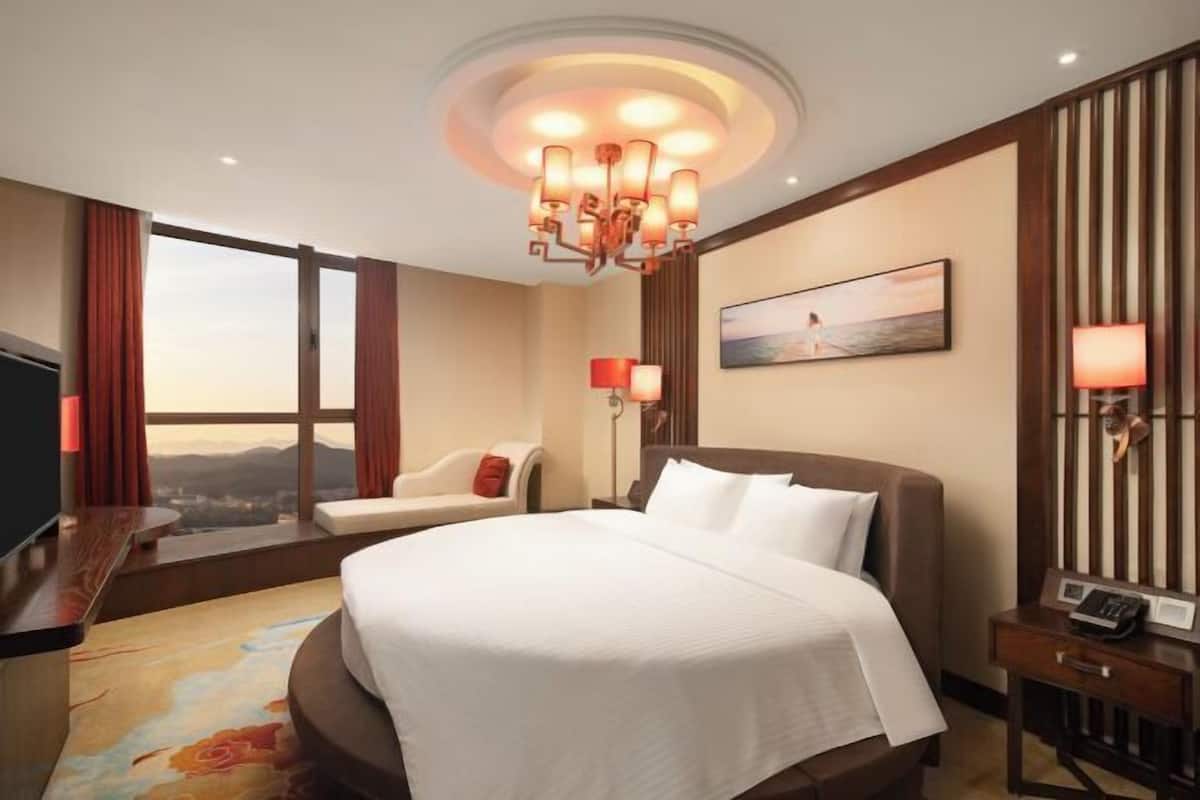 Une chambre d’hôtel avec un grand lit, un bureau, une chaise, une télévision, un tableau, une lampe et une vue sur les montagnes.