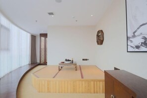 Una habitación minimalista con un suelo de tatami, una mesa de madera con un cuenco y una obra de arte grande enmarcada en la pared.