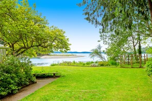 A grassy area with a bench and a path leading to a body of water. - Waterfront retreat with private beach, cookhouse, hot tub, EV charger, & firepit (Gig Harbor)