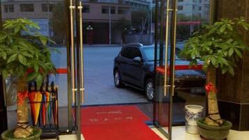 A hotel entrance with a red carpet, glass doors, and potted plants.