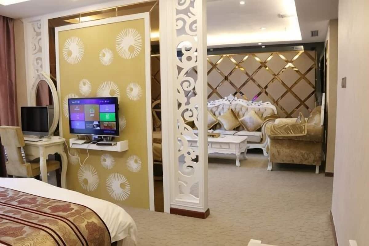 A hotel room with a bed, a TV, a desk, and a seating area with a sofa and armchairs.