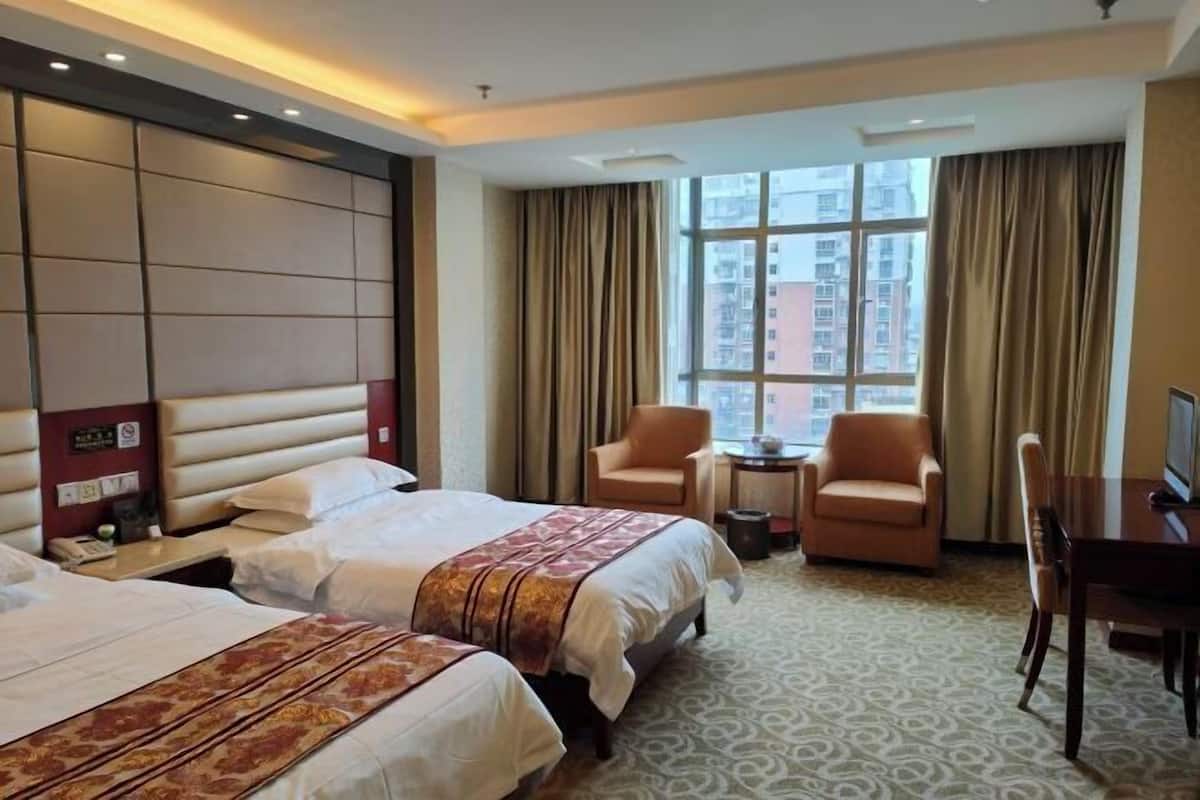 A hotel room with two beds, a desk, a chair, and a small table.