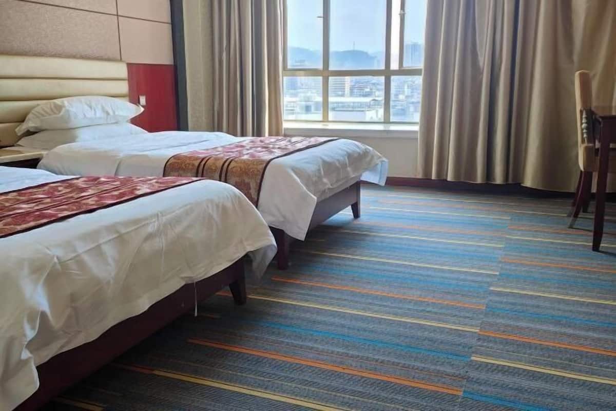 A hotel room with two beds, a large window with a city view, and a colorful striped carpet.