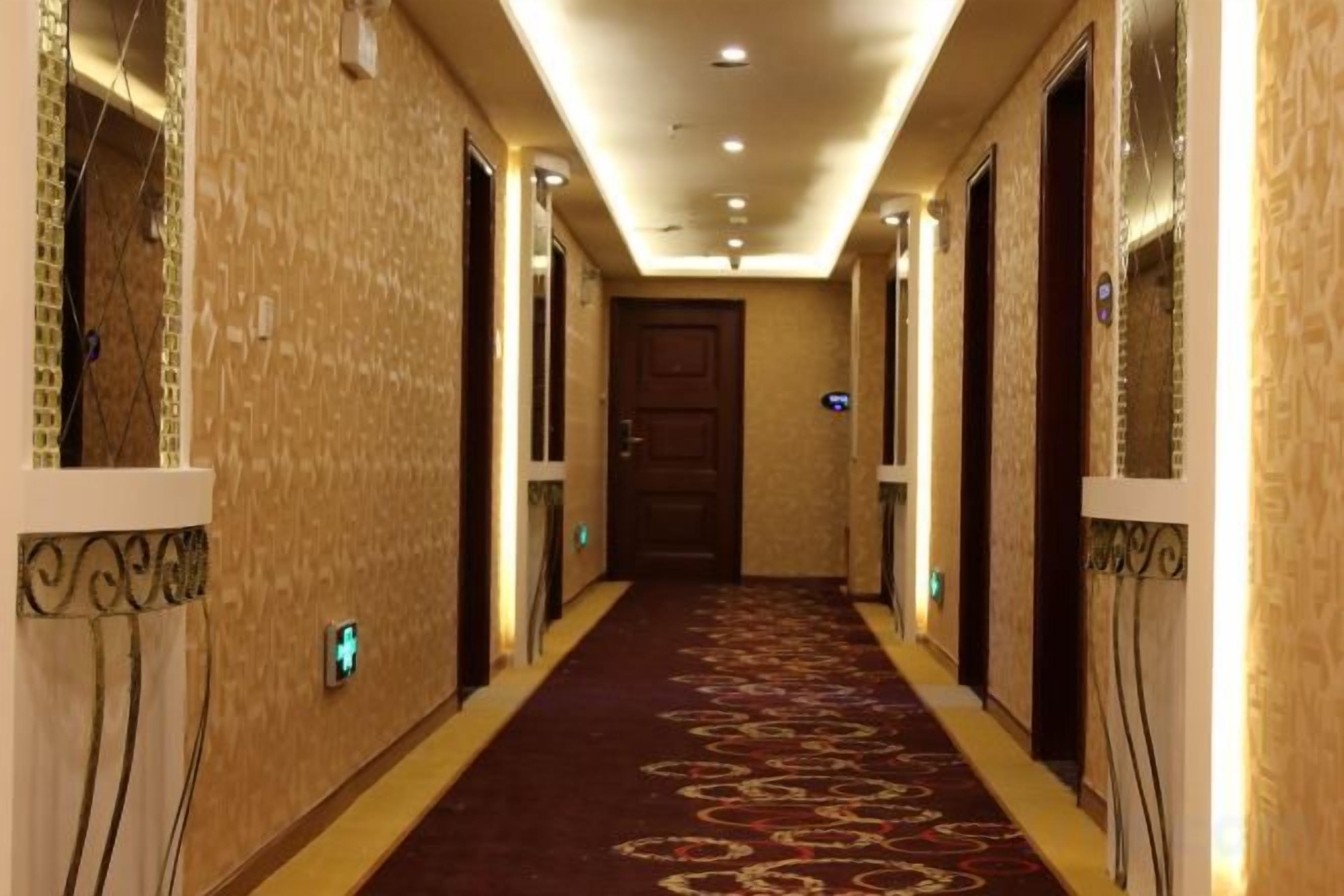 Un pasillo de hotel con piso alfombrado, puertas a ambos lados y una lámpara en el techo.