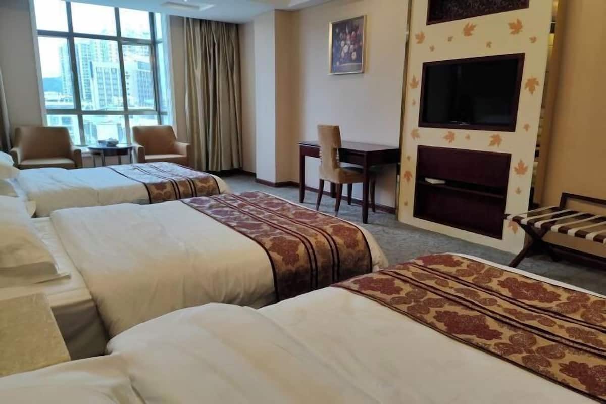A hotel room with three beds, a desk, a chair, a television, and a large window with curtains.
