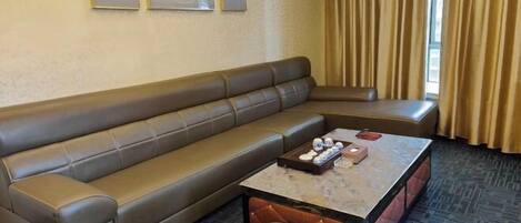 A hotel room with a brown leather sofa, a marble coffee table, and a trash can.