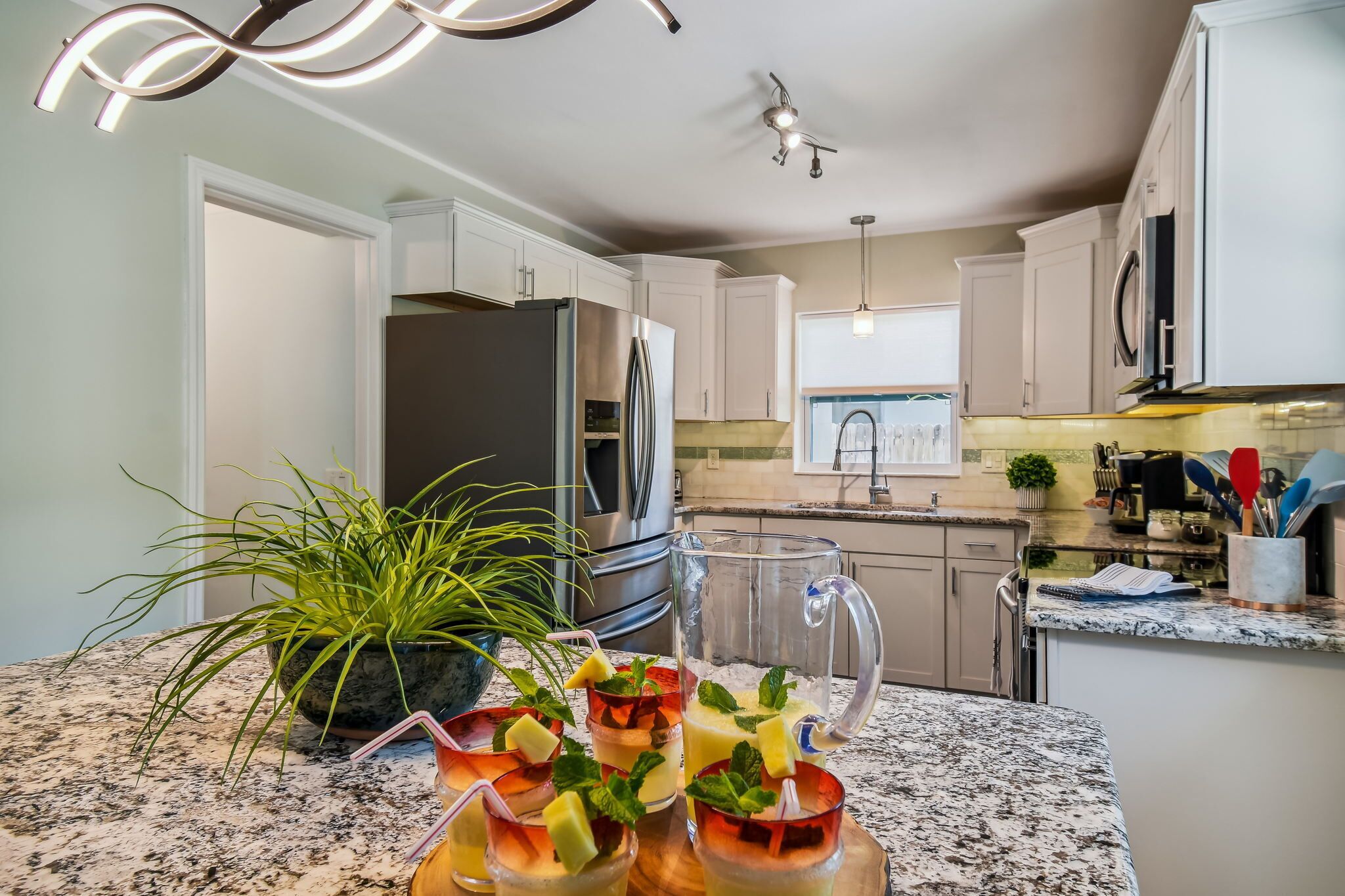 A kitchen with white cabinets, a stainless steel refrigerator, a granite countertop, and a potted plant.