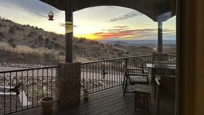 A wooden deck with outdoor seating, overlooking a landscape with hills and a sunset. - 60-acre custom home with breathtaking views of city of Las Cruces & Organs! (Las Cruces)