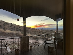 Un terrazzo in legno con posti a sedere all'aperto, affacciato su un paesaggio collinare e un tramonto.