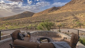 A patio with outdoor seating and a fire pit, surrounded by a metal railing, overlooking a desert landscape with hills. - 60-acre custom home with breathtaking views of city of Las Cruces & Organs! (Las Cruces)