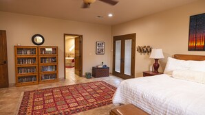 A bedroom with a large bed, a ceiling fan, a bookshelf, and a door leading to another room. - 60-acre custom home with breathtaking views of city of Las Cruces & Organs! (Las Cruces)