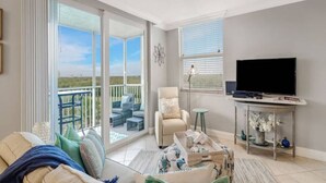 A living room with a sofa, a TV, and a balcony with outdoor furniture.