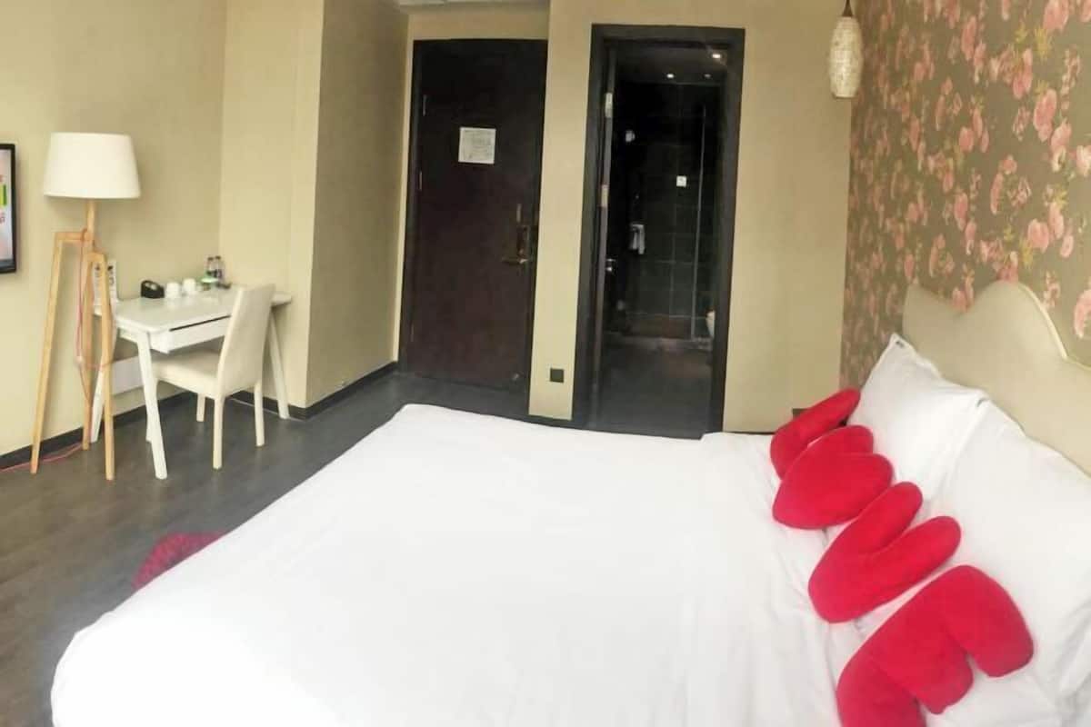 A hotel room with a bed, a desk, a chair, and a door leading to a bathroom.