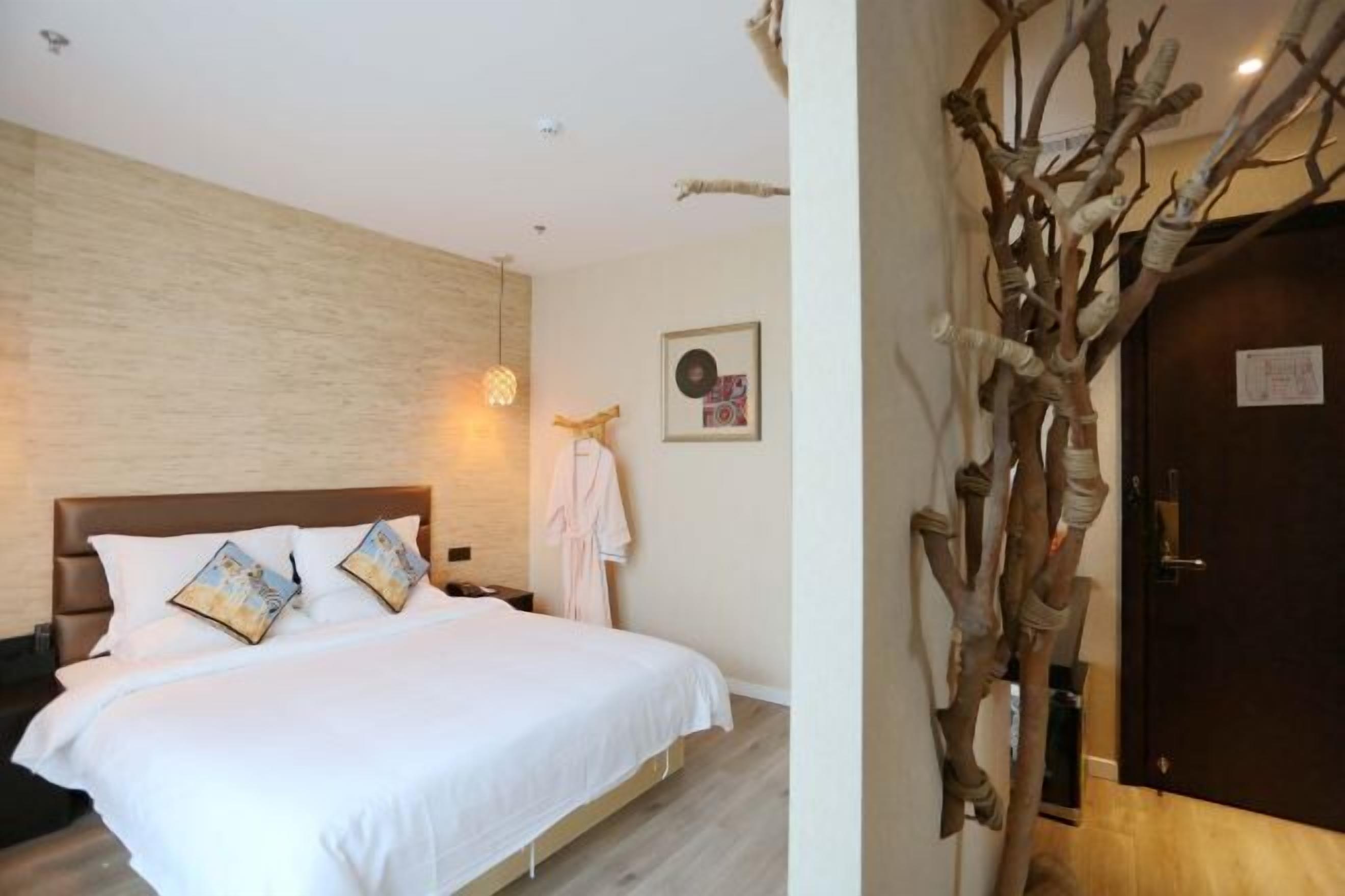 A hotel room with a large bed, a wooden headboard, a wall-mounted light fixture, and a decorative tree branch.