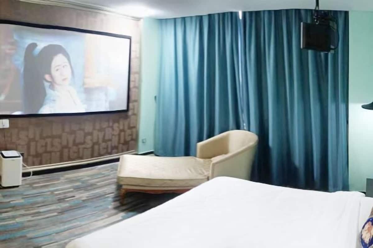 A hotel room with a bed, a TV screen, a chair, and a curtain.