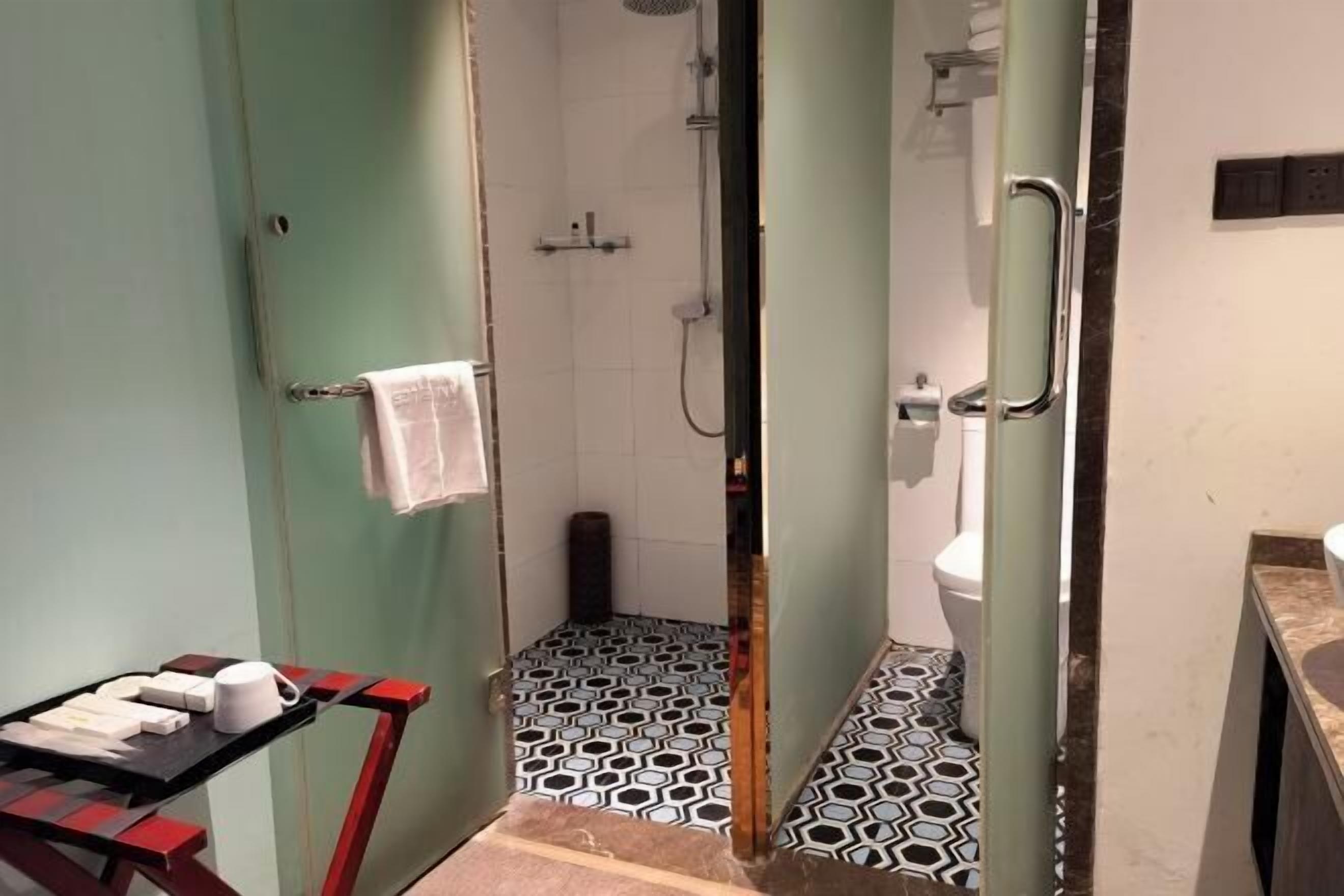 Une salle de bain avec douche, toilettes et lavabo. On y trouve un porte-serviettes et une petite table avec des articles de toilette.