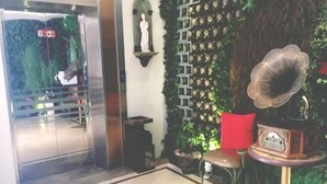 A reception area with a glass elevator, a wall-mounted statue, a decorative wall with a floral pattern, a red chair, and a vintage radio on a small table. - Sotel Inn (Wenzhou Xincheng Convention and Exhibition Center) (Wenzhou)