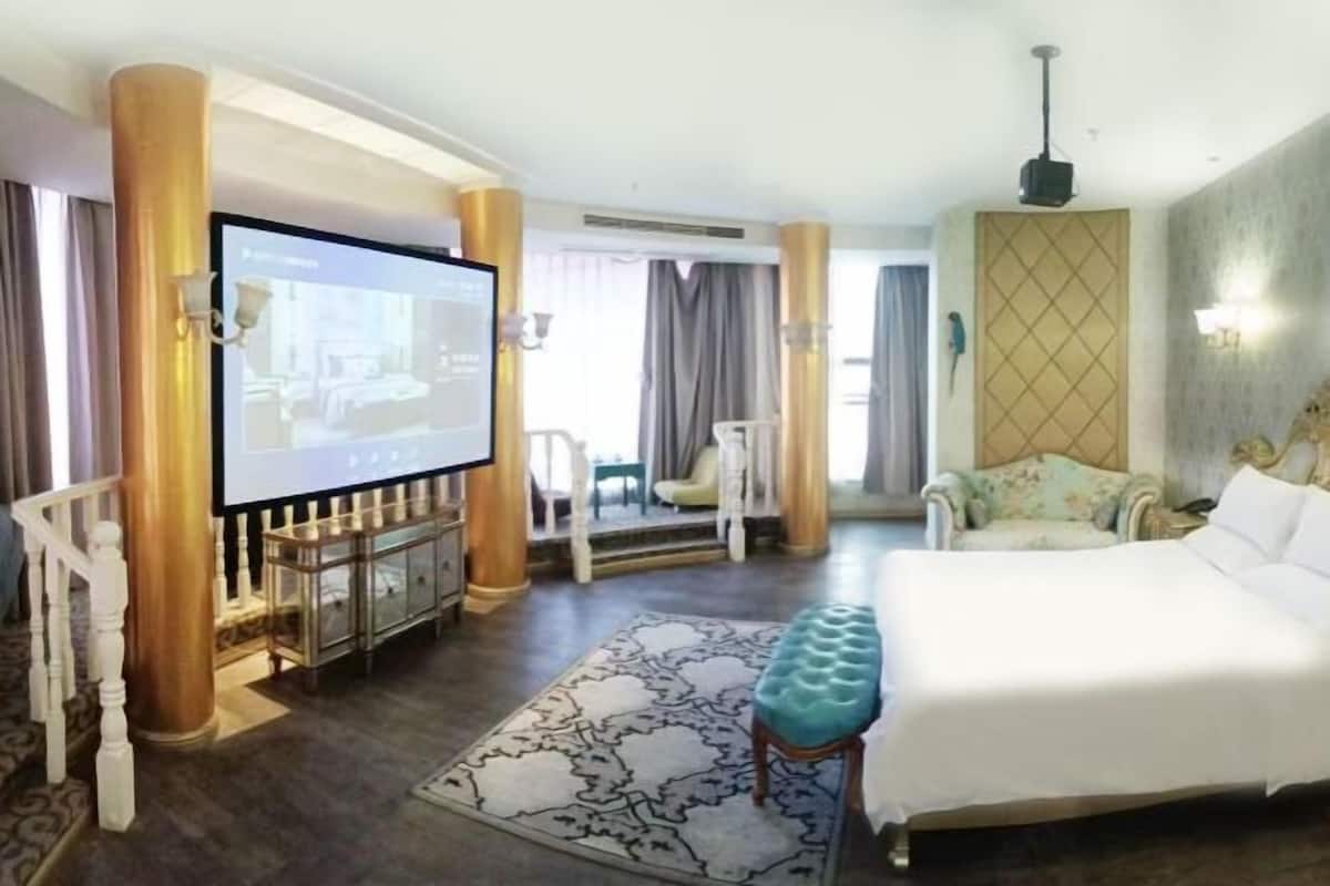 A hotel room with a large bed, a television, a seating area with a chair, and a decorative wall.