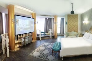 Habitación de hotel con una cama grande, televisión, zona de estar con una silla y un adorno en la pared.