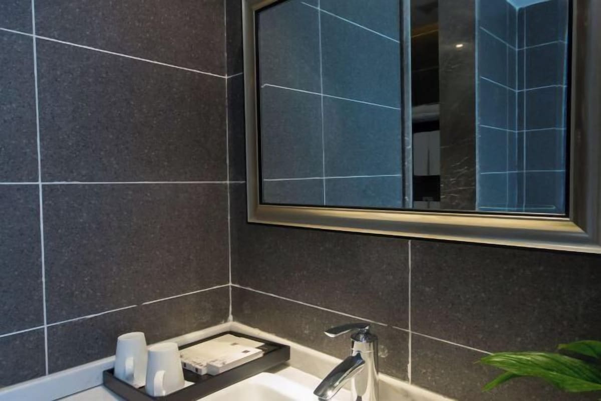 Un baño con baldosas oscuras, un espejo, un lavabo y una planta.