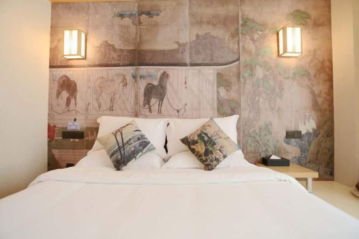 A bed with white bedding, two pillows, and a headboard with a mural. There are two wall-mounted light fixtures on either side of the headboard.
