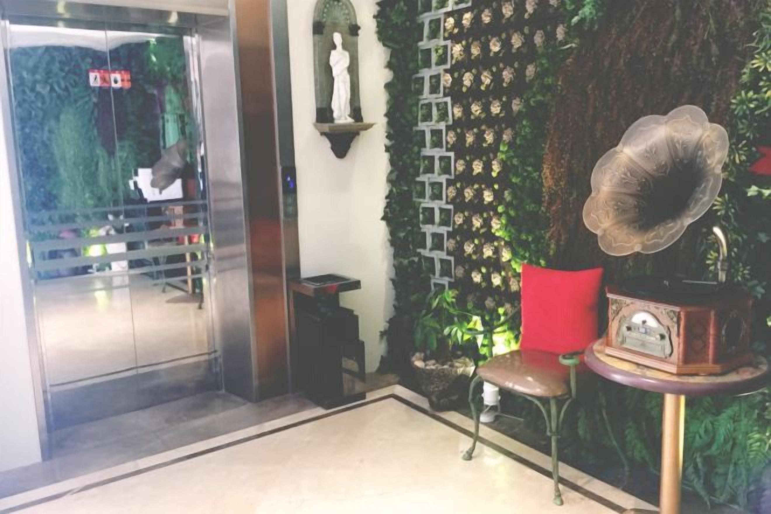 An indoor area with a glass elevator, a red chair, a wall with a floral pattern, and a vintage gramophone.