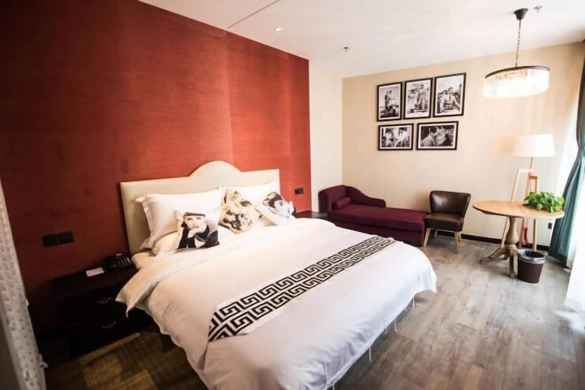 A hotel room with a bed, a desk, a chair, a lamp, and framed pictures on the wall.