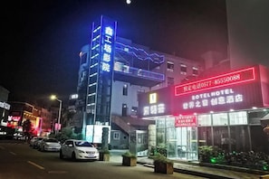 Un hotel con un letrero llamativo, una escalera que conduce a la entrada y una fila de coches aparcados.