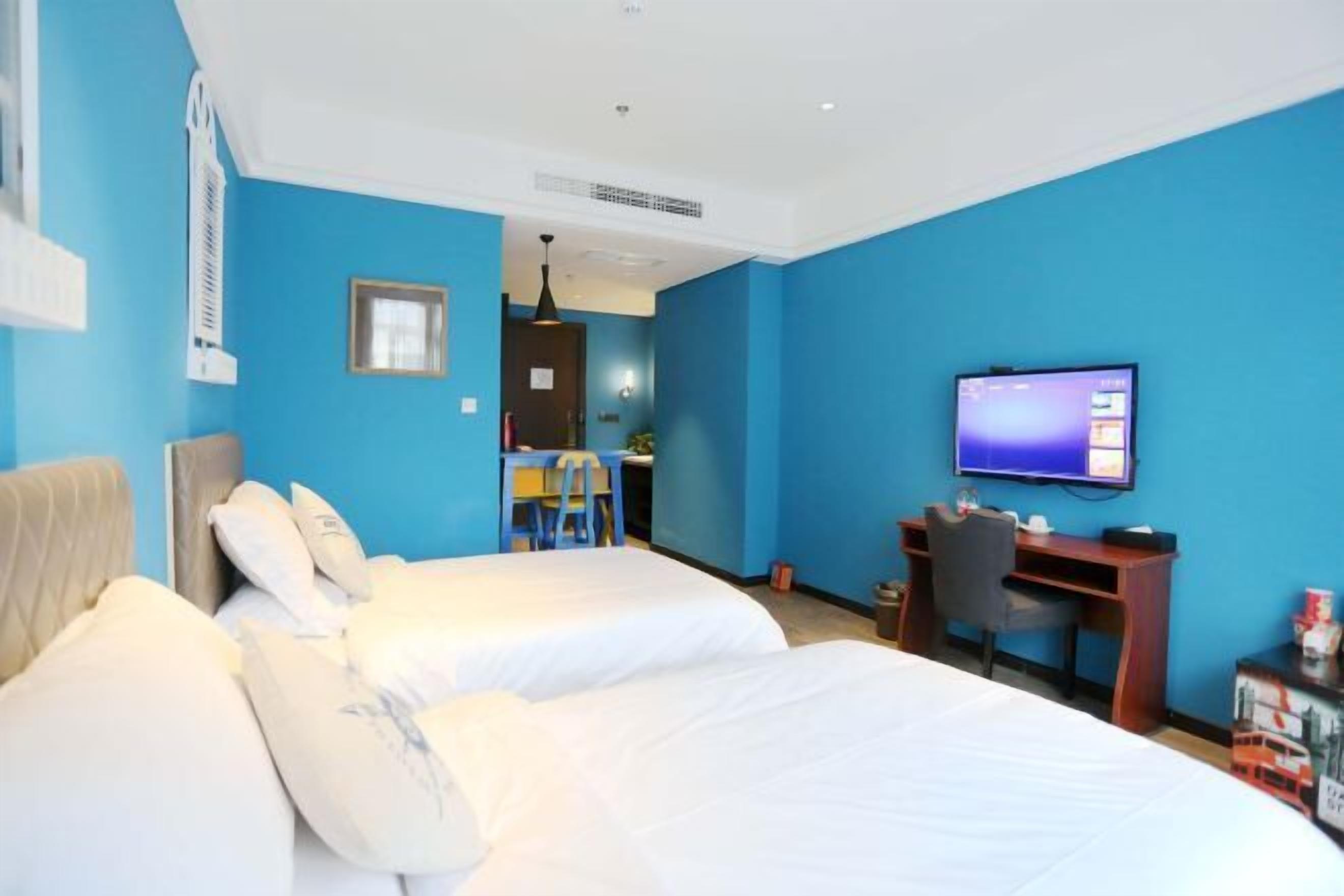A hotel room with two beds, a desk, a chair, a television, and a small table.