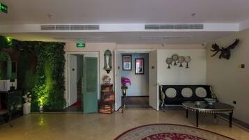 A hotel lobby with a reception desk, a green wall, a sofa, and a patterned rug.
