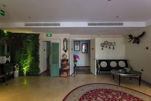 Un vestíbulo de hotel con una recepción, una pared verde, un sofá y una alfombra estampada.