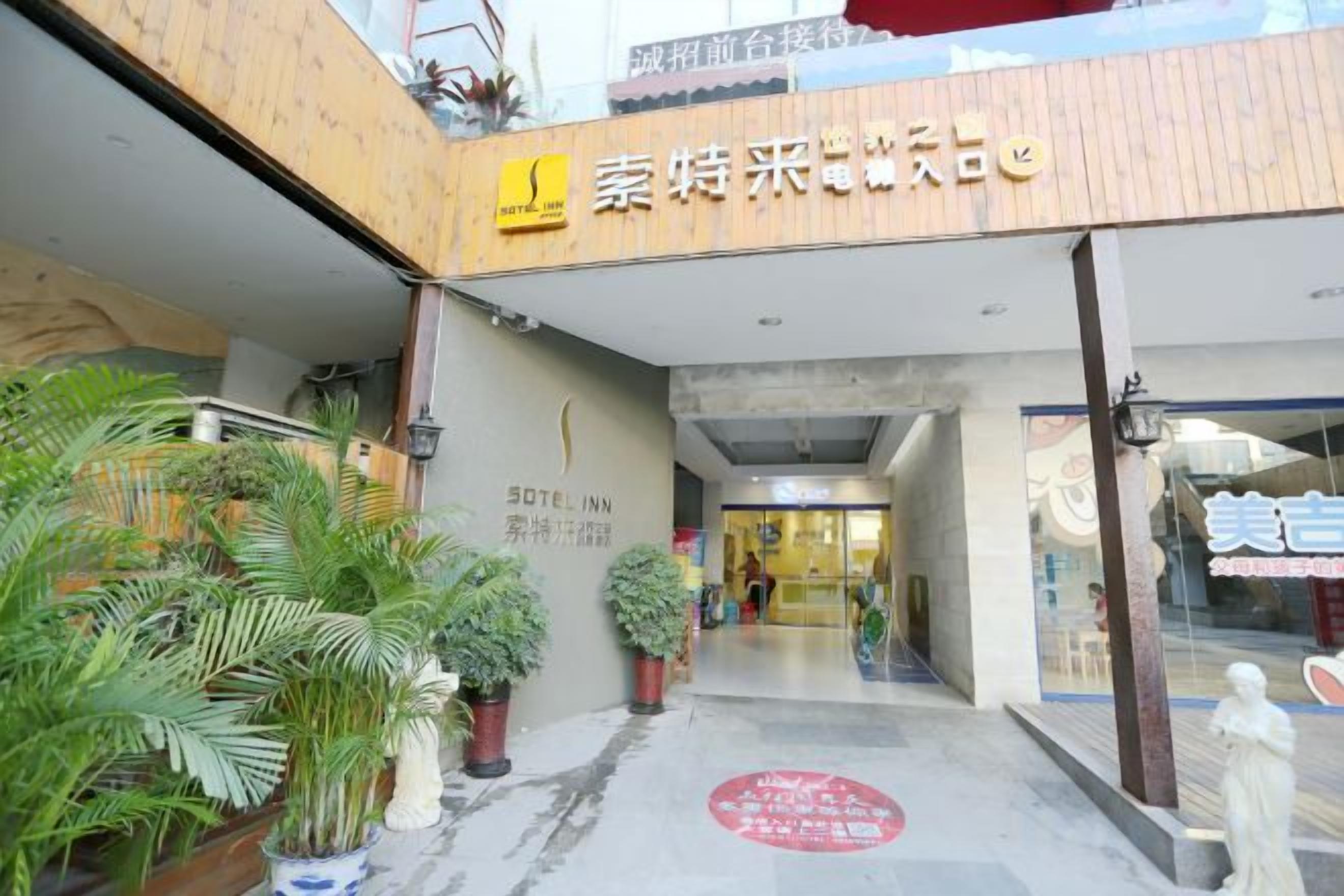A hotel entrance with a signboard, potted plants, and a statue.