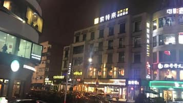 Un immeuble à plusieurs étages, doté d’une enseigne lumineuse, avec une rue devant et des voitures garées.